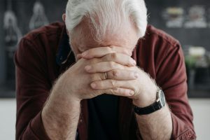 Elderly man with white hair contemplating past memories through a photo album at home.